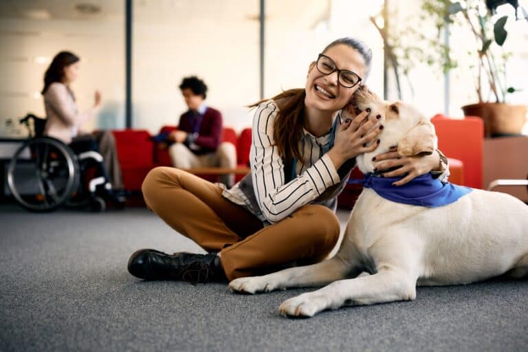 A young woman sitting on the floor with her dog licking her face