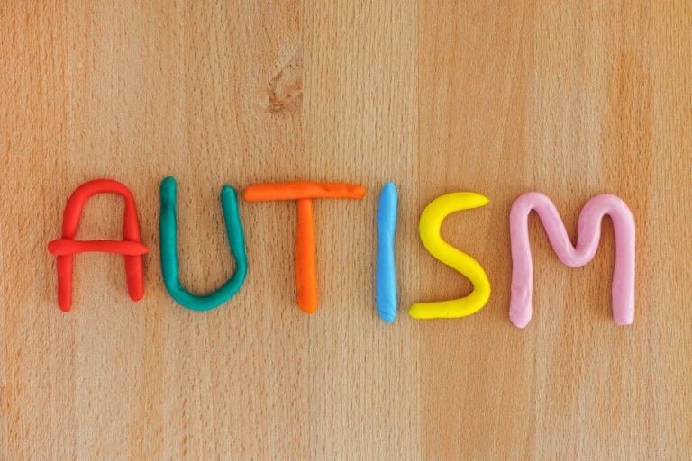 Colorful clay lettering of 'autism' on wood surface.