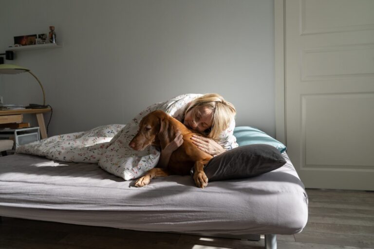 Woman lovingly hugging her pet dog while lying in bed.